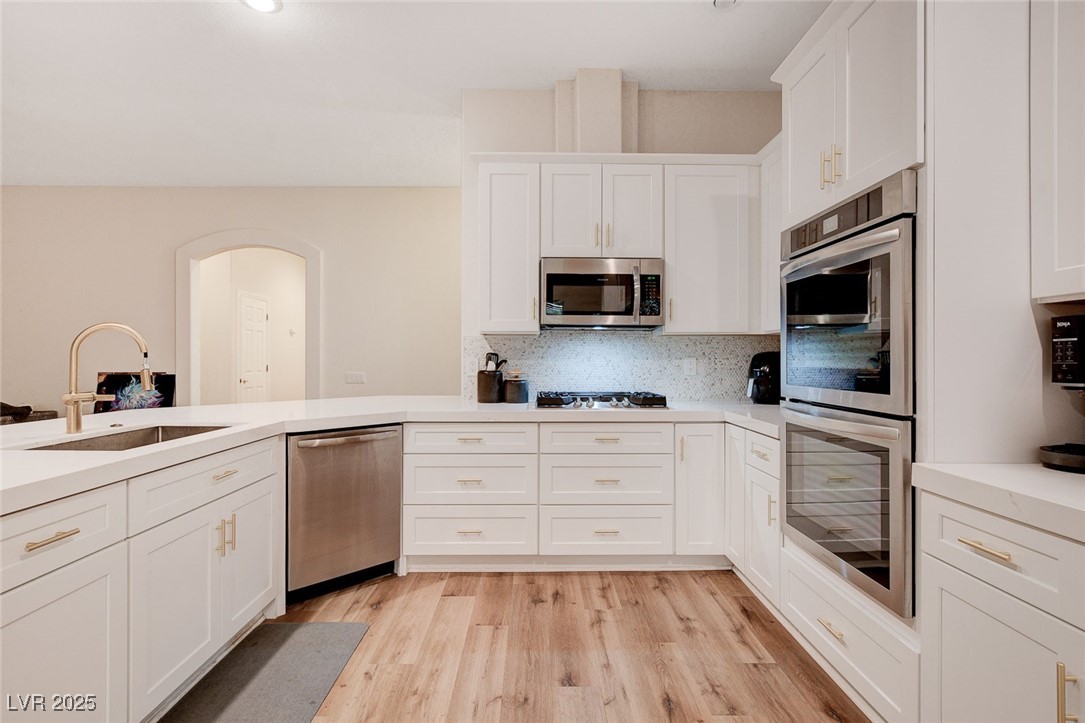 10720 Elm Ridge Avenue Las Vegas, NV 89144 - Photo 12 of 67 Kitchen featuring appliances with stainless steel finishes, tasteful backsplash, white cabinetry, and light wood-style floors