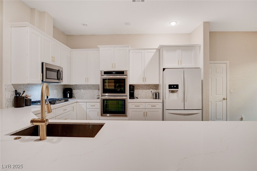 10720 Elm Ridge Avenue Las Vegas, NV 89144 - Photo 13 of 67 Kitchen with appliances with stainless steel finishes, white cabinets, tasteful backsplash, light stone counters, and recessed lighting