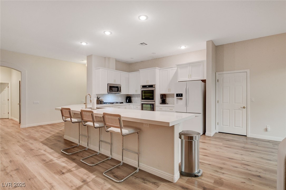 10720 Elm Ridge Avenue Las Vegas, NV 89144 - Photo 5 of 67 Kitchen with a breakfast bar, light countertops, arched walkways, appliances with stainless steel finishes, and white cabinetry