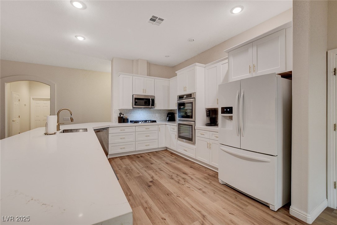 10720 Elm Ridge Avenue Las Vegas, NV 89144 - Photo 6 of 67 Kitchen with appliances with stainless steel finishes, white cabinetry, backsplash, light wood-style flooring, and a peninsula