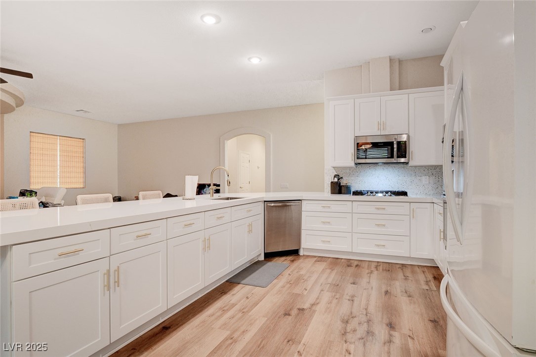 10720 Elm Ridge Avenue Las Vegas, NV 89144 - Photo 8 of 67 Kitchen with appliances with stainless steel finishes, white cabinetry, arched walkways, light wood-style floors, and backsplash