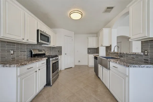 a large kitchen with granite countertop a sink a stove top oven and white cabinets
