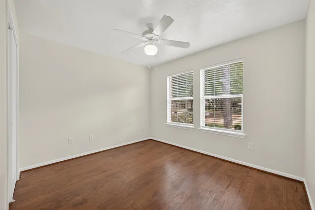 an empty room with wooden floor fan and windows