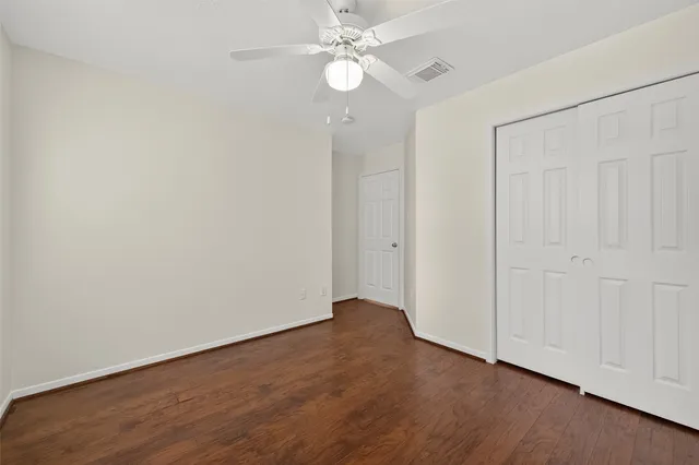 an empty room with wooden floor fan and windows
