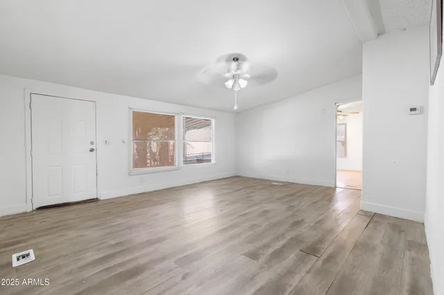 an empty room with chandelier fan and windows