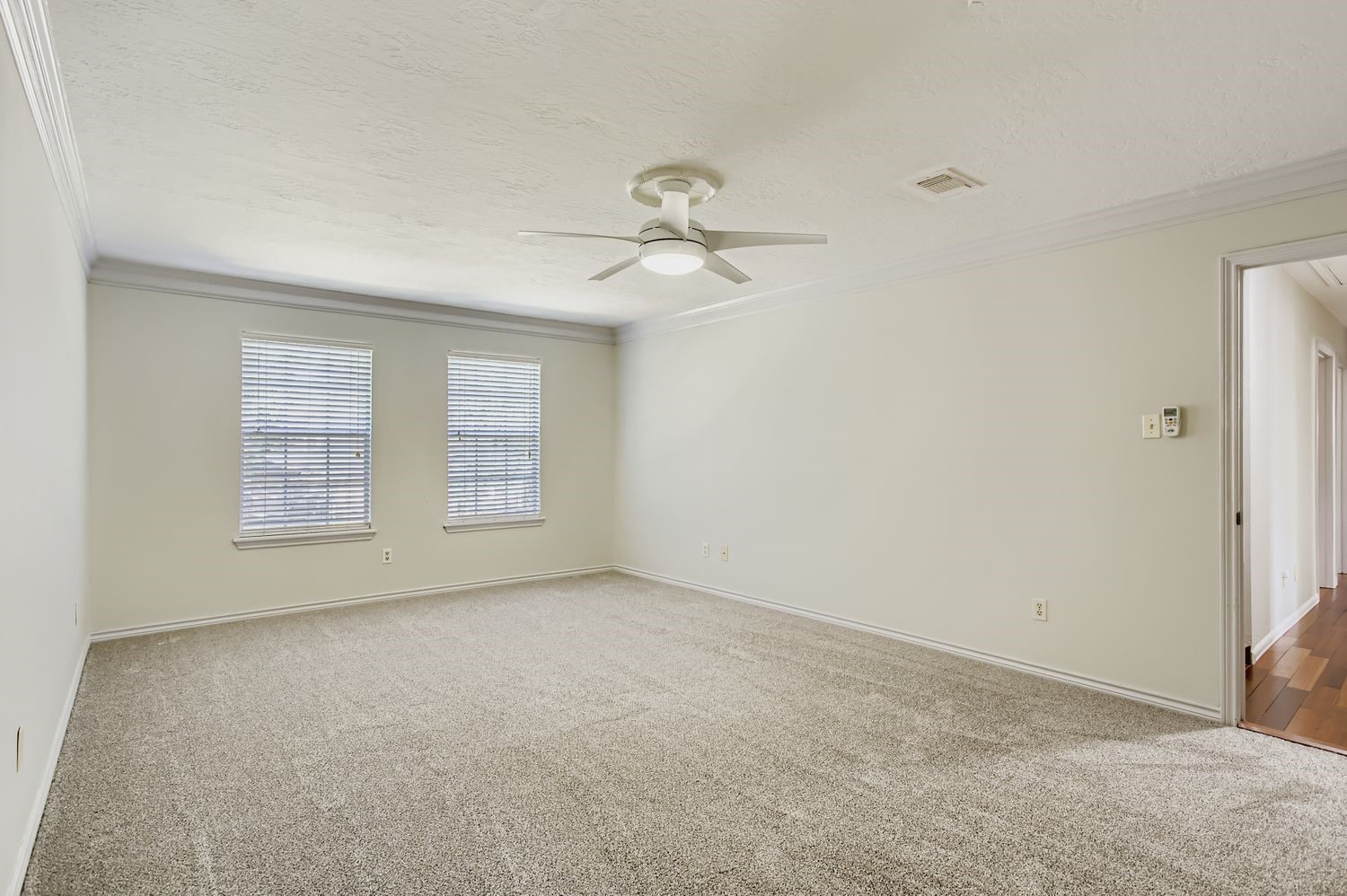 8518 Rebawood Drive Humble, TX 77346 - Photo 16 of 36 Spacious and inviting, this primary bedroom features carpeting, abundant natural light from two large windows, and a sleek ceiling fan, creating a serene retreat.