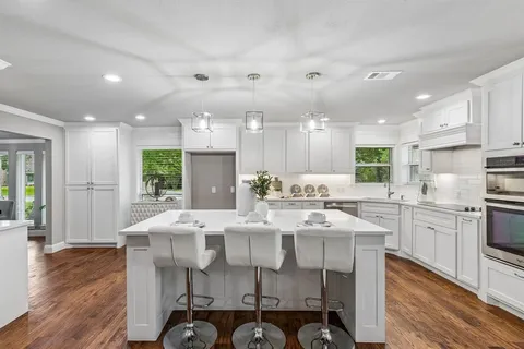 a kitchen with stainless steel appliances kitchen island granite countertop a stove a sink a refrigerator and white cabinets with wooden floor