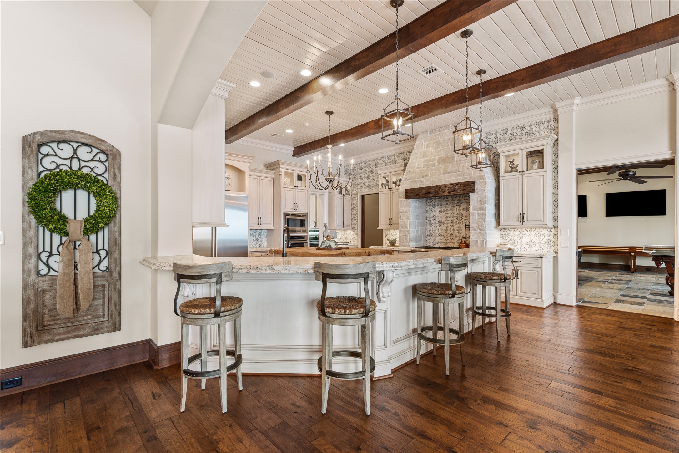 12349 Longmire Trace Conroe, TX 77304 - Photo 7 of 48 Chef’s kitchen stuns with exposed beams, stone vent hood, oversized island, and custom cabinetry.
