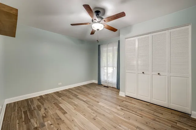 an empty room with wooden floor fan and windows