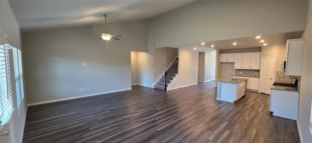 a view of an empty room and kitchen with wooden floor