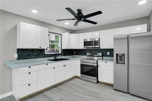 a kitchen with granite countertop a refrigerator a sink and white cabinets
