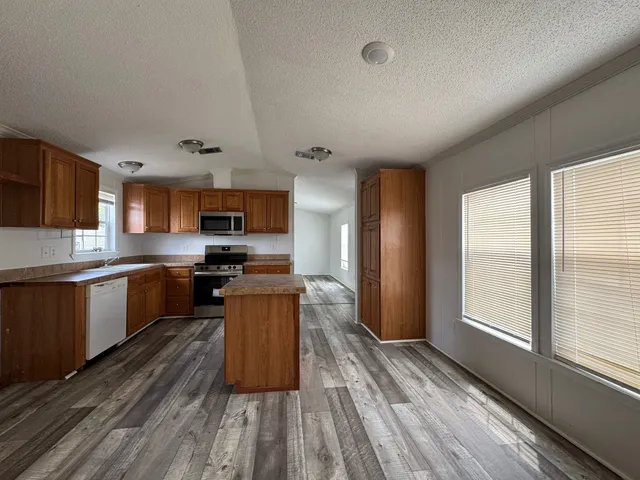 a kitchen with stainless steel appliances granite countertop a refrigerator a stove top oven a sink dishwasher and wooden cabinets with wooden floor