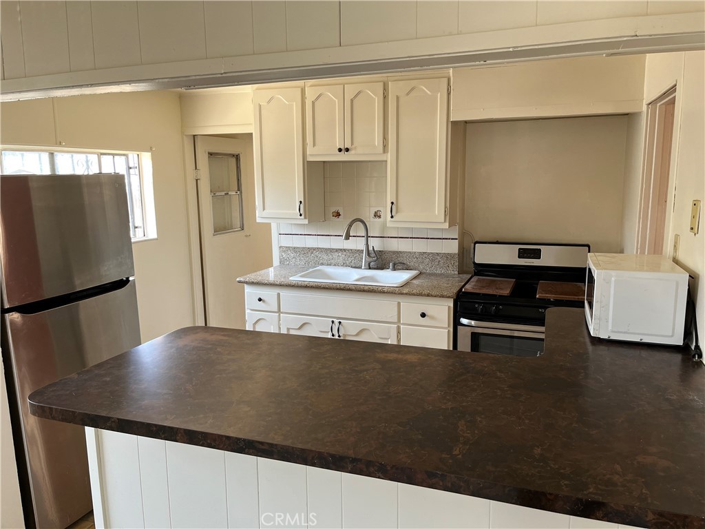7763 Compton Avenue Los Angeles, CA 90001 - Photo 11 of 20 a kitchen with stainless steel appliances a stove a refrigerator a sink and white cabinets with wooden floor