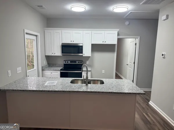 a kitchen with kitchen island granite countertop a sink a microwave a refrigerator and cabinets