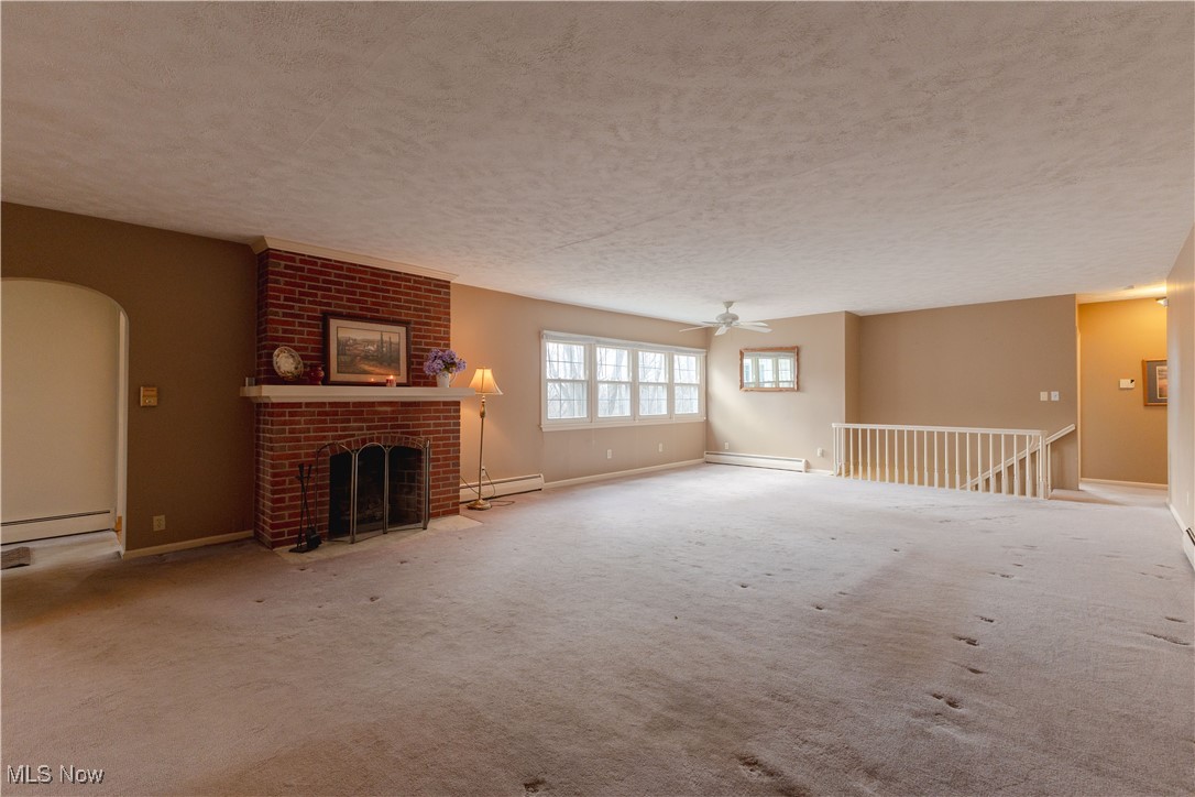 1639 South Ridge Road West Ashtabula, OH 44004 - Photo 29 of 44 Unfurnished living room with baseboards, a textured ceiling, a brick fireplace, ceiling fan, and a baseboard radiator