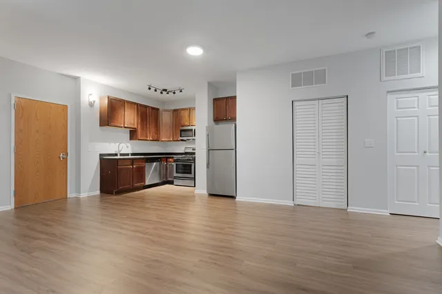 a view of kitchen with stainless steel appliances wooden floor and an empty room