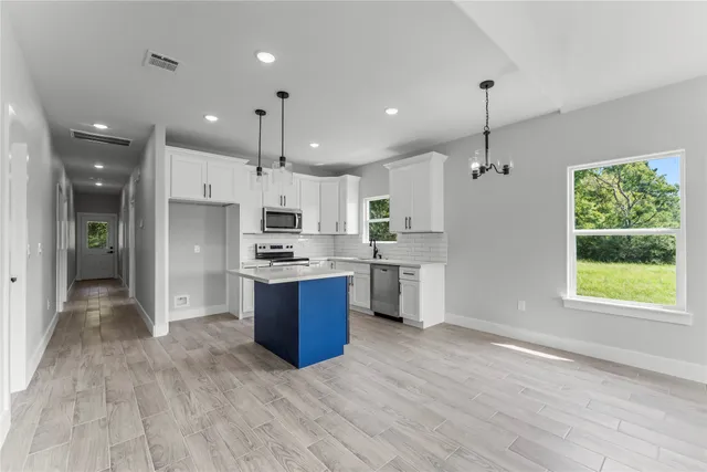 a kitchen with stainless steel appliances kitchen island granite countertop a refrigerator a sink dishwasher a oven and a dining table with wooden floor