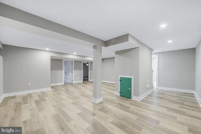 a view of an empty room with wooden floor and kitchen space