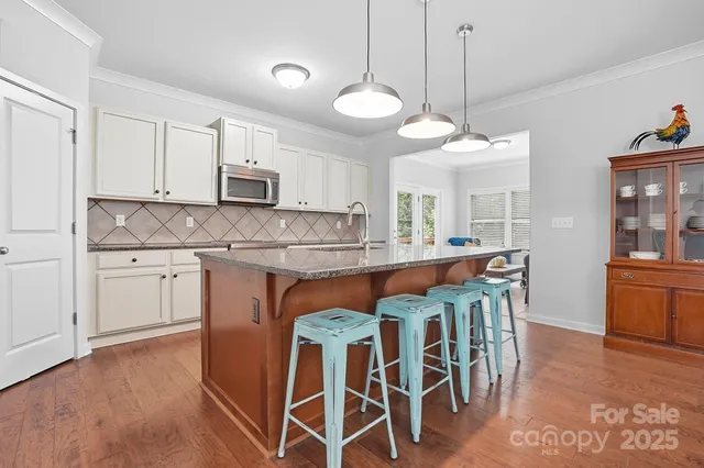 a kitchen with stainless steel appliances granite countertop a stove top oven a refrigerator a sink and a dining table with white cabinets