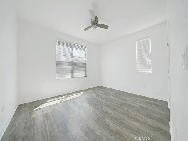 an empty room with wooden floor chandelier fan and windows