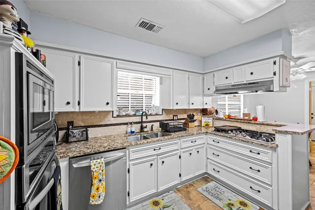 a kitchen with granite countertop a sink cabinets stainless steel appliances and a window