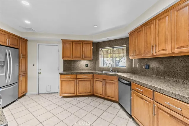 a kitchen with stainless steel appliances granite countertop a sink and dishwasher a refrigerator with wooden cabinets