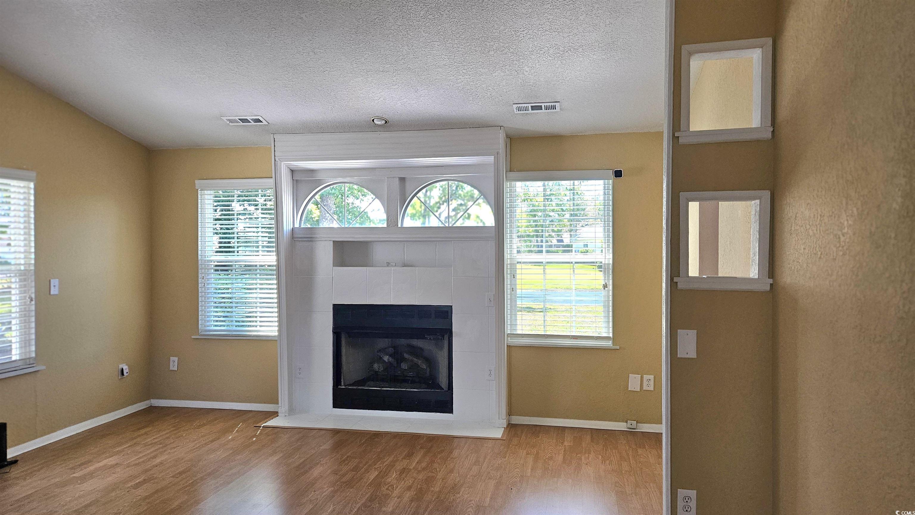 545 Saluda River Road Myrtle Beach, SC 29588 - Photo 6 of 25 Unfurnished living room with plenty of natural light, wood finished floors, a tile fireplace, and a textured ceiling