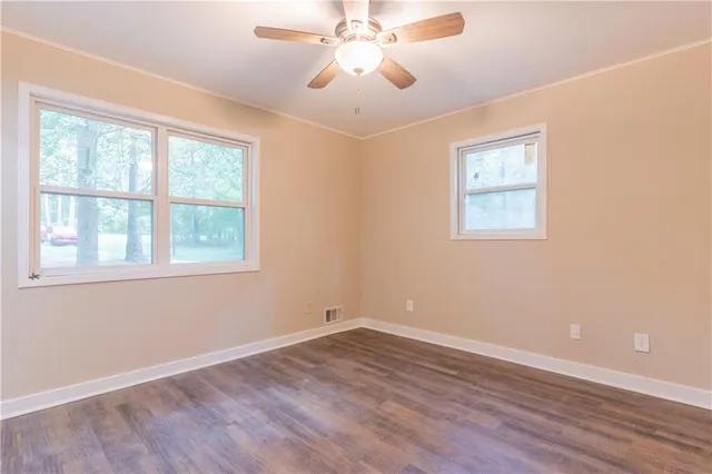an empty room with wooden floor chandelier fan and windows