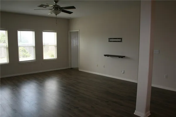 an empty room with wooden floor fan and windows