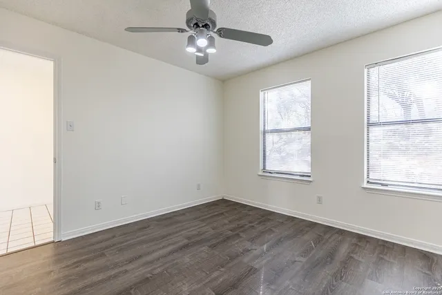 a view of empty room with wooden floor and fan