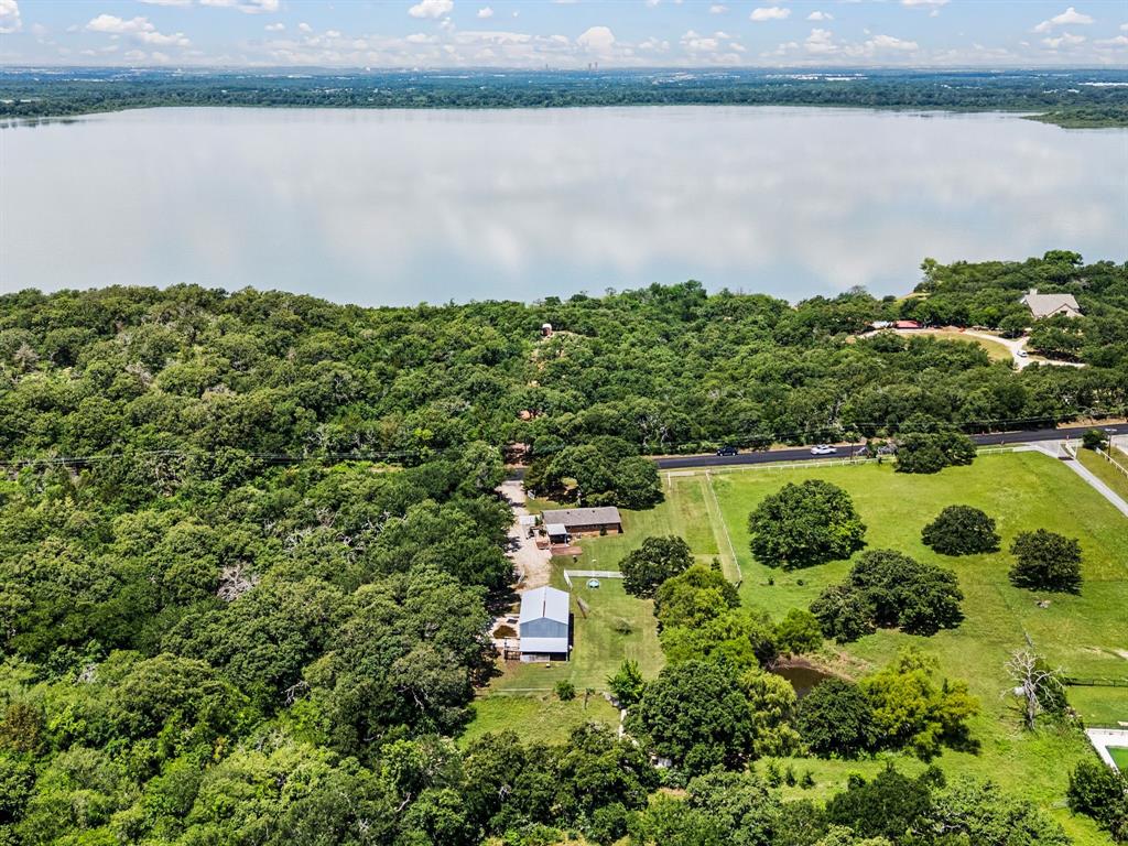 3900 Moseley Road Cross Roads, TX 76227 - Photo 2 of 36 Expansive property featuring a tranquil body of water, mature tree coverage, a large metal-roofed building, and open grassy areas with scattered trees