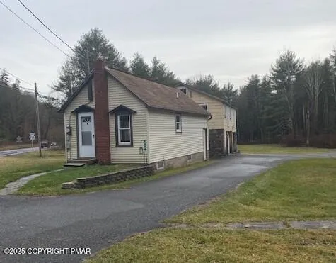 a view of a small white house next to a yard and large trees