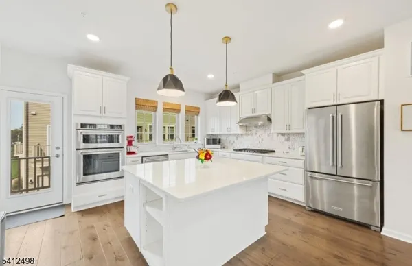 a kitchen with stainless steel appliances a stove a sink a refrigerator a center island and a wooden floor