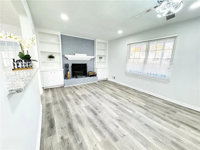 a view of a livingroom with a fireplace a ceiling fan and windows