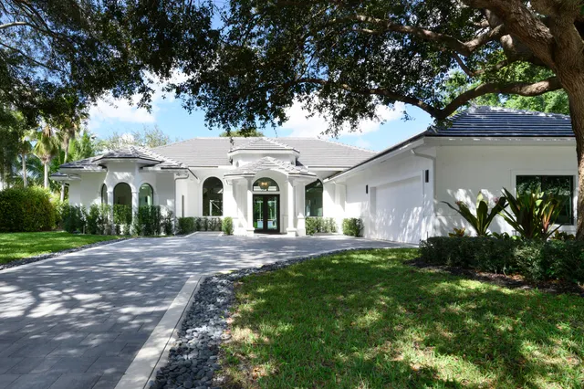 a view of a white house with a big yard plants and large tree