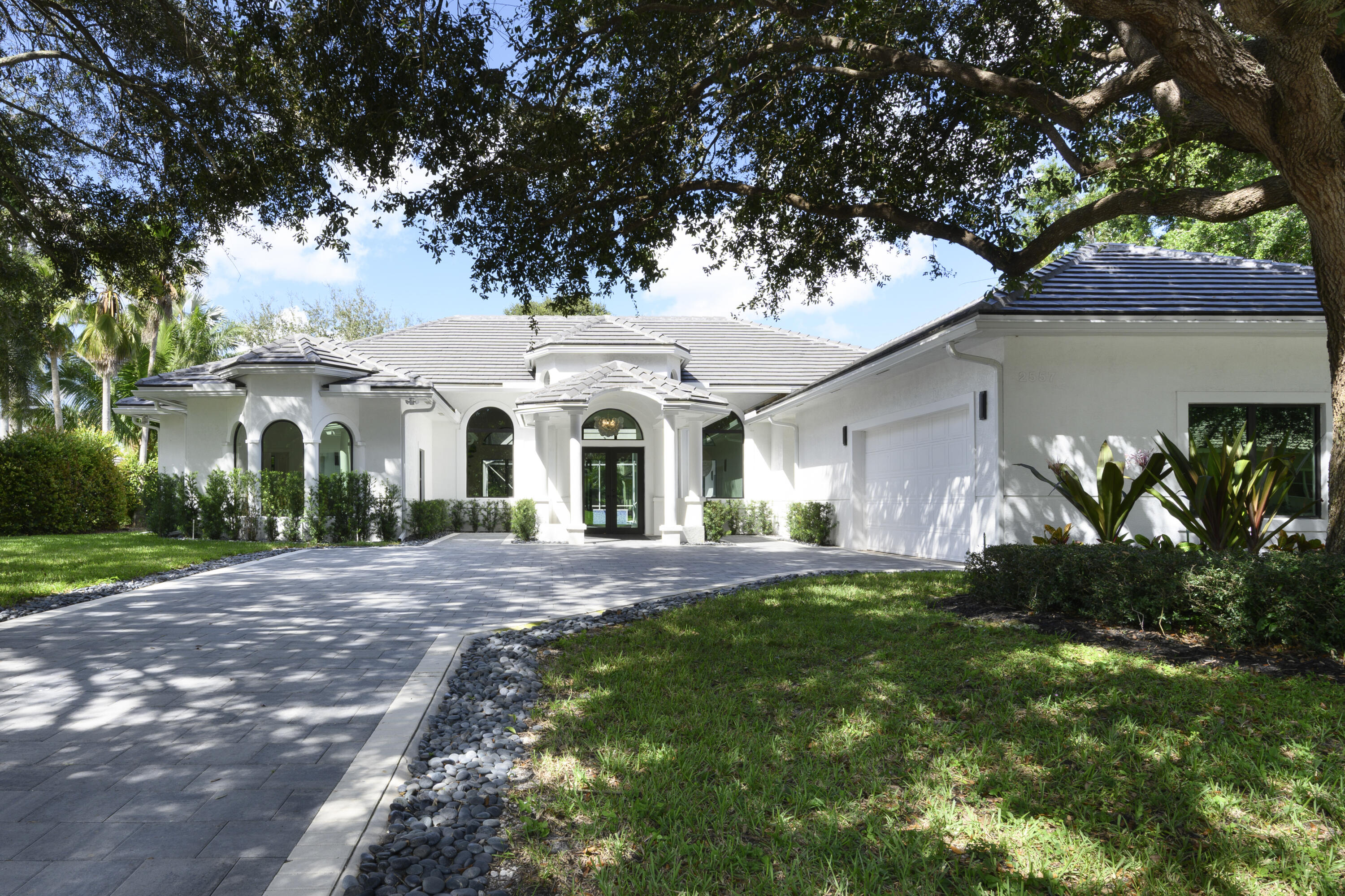 a view of a white house with a big yard plants and large tree