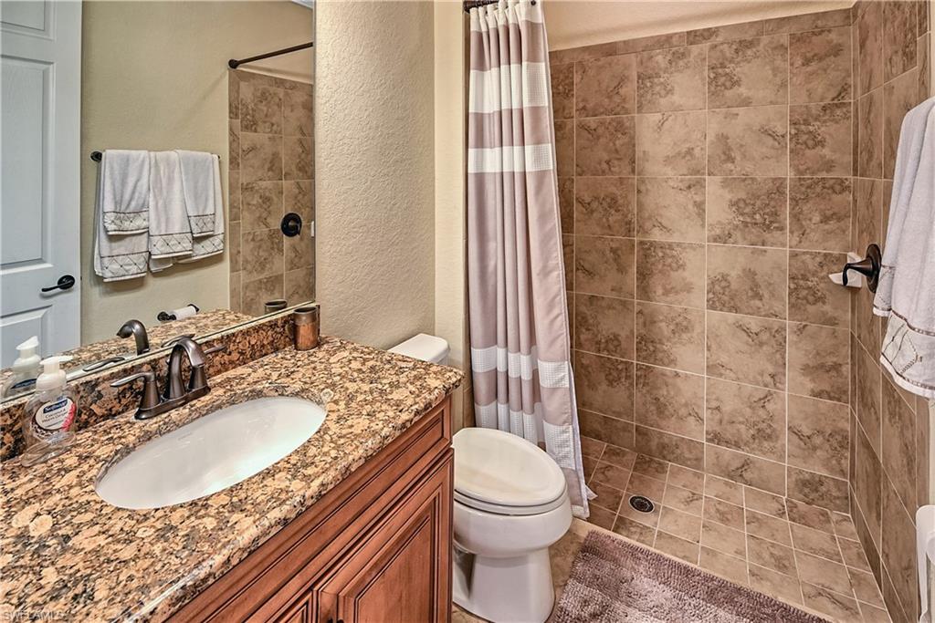 9215 Veneto Lane Naples, FL 34113 - Photo 14 of 34 a bathroom with a granite countertop sink toilet a mirror and shower