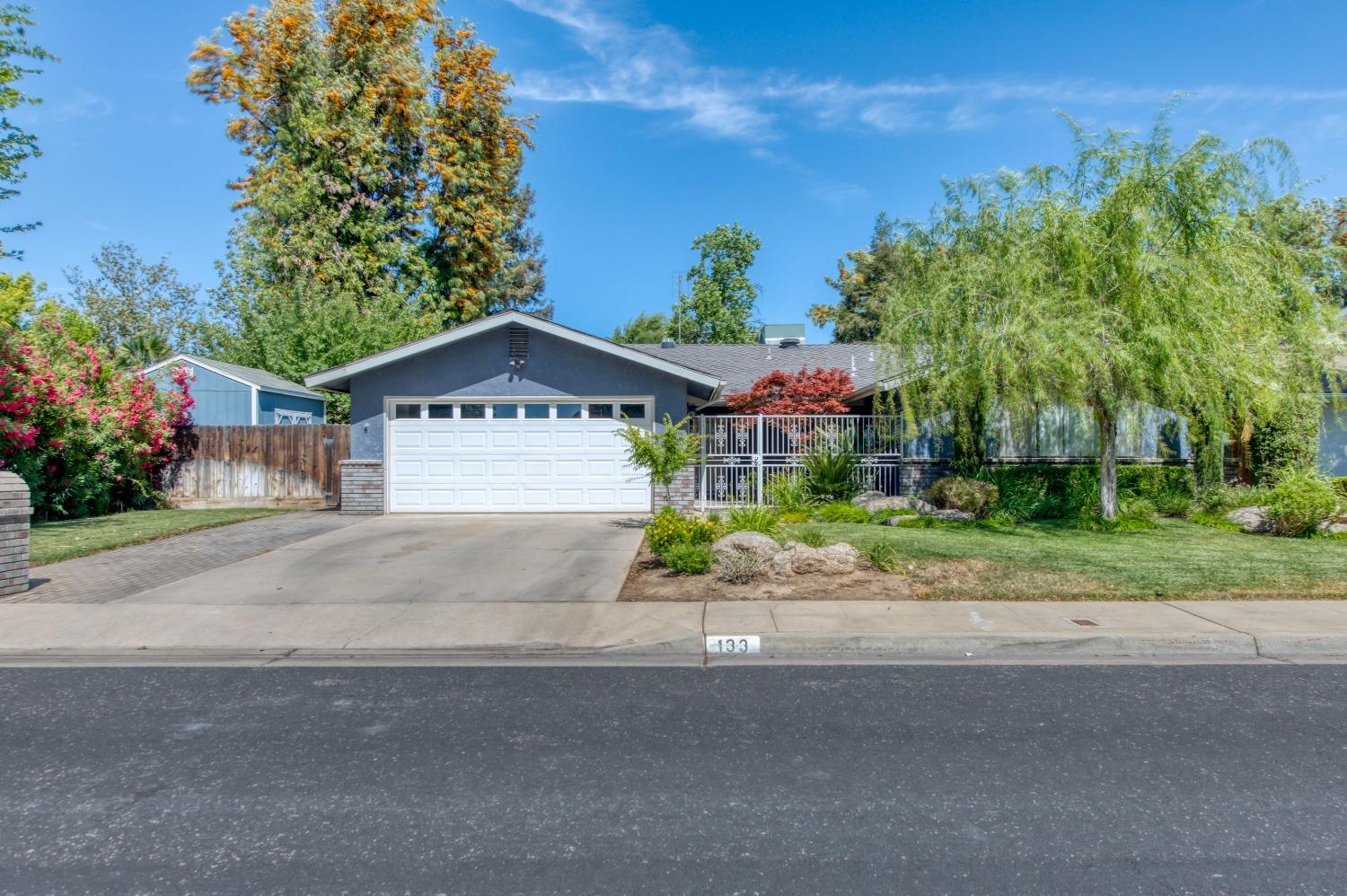 a sign board with flower plants and large trees