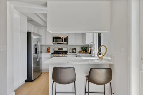 a kitchen with stainless steel appliances a dining table chairs refrigerator and sink