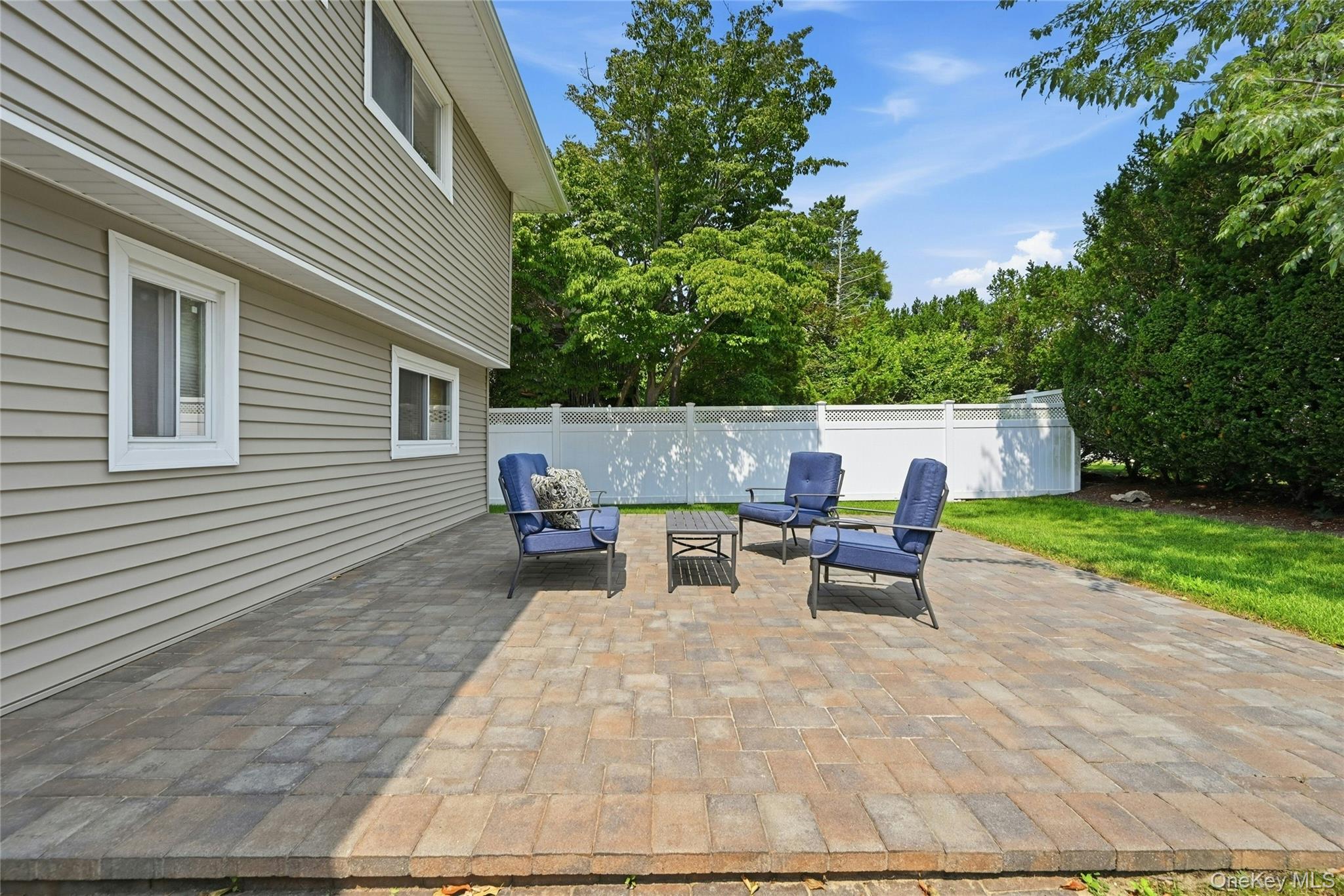 3165 Clubhouse Road Merrick, NY 11566 - Photo 38 of 45 Expansive paver patio with a low retaining wall, bordered by a manicured lawn and a white privacy fence