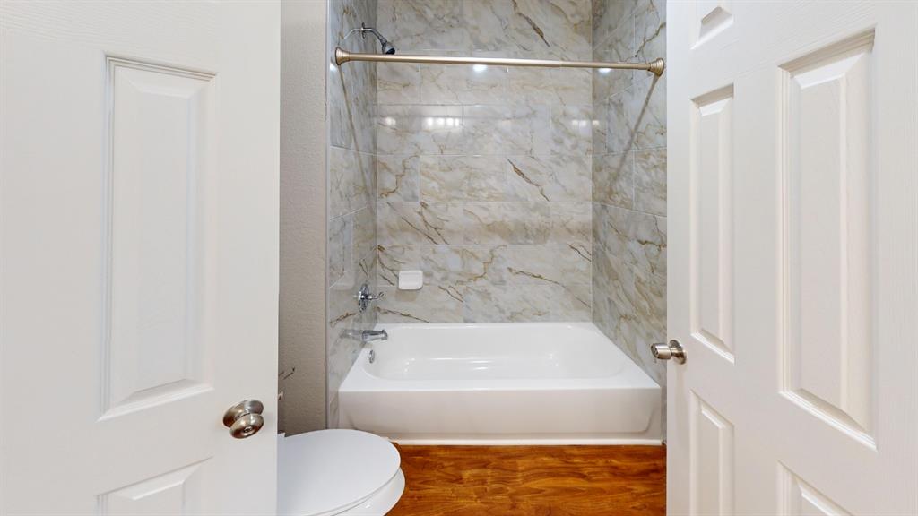 7913 Rice Drive Rowlett, TX 75088 - Photo 20 of 25 Bathroom featuring a white bathtub, light-toned tiled shower surround, chrome fixtures, and wood-finish flooring