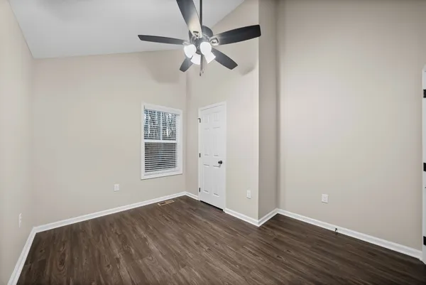 an empty room with wooden floor chandelier fan and windows
