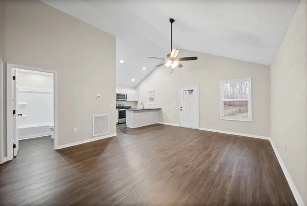 a view of an empty room with wooden floor kitchen view and a window