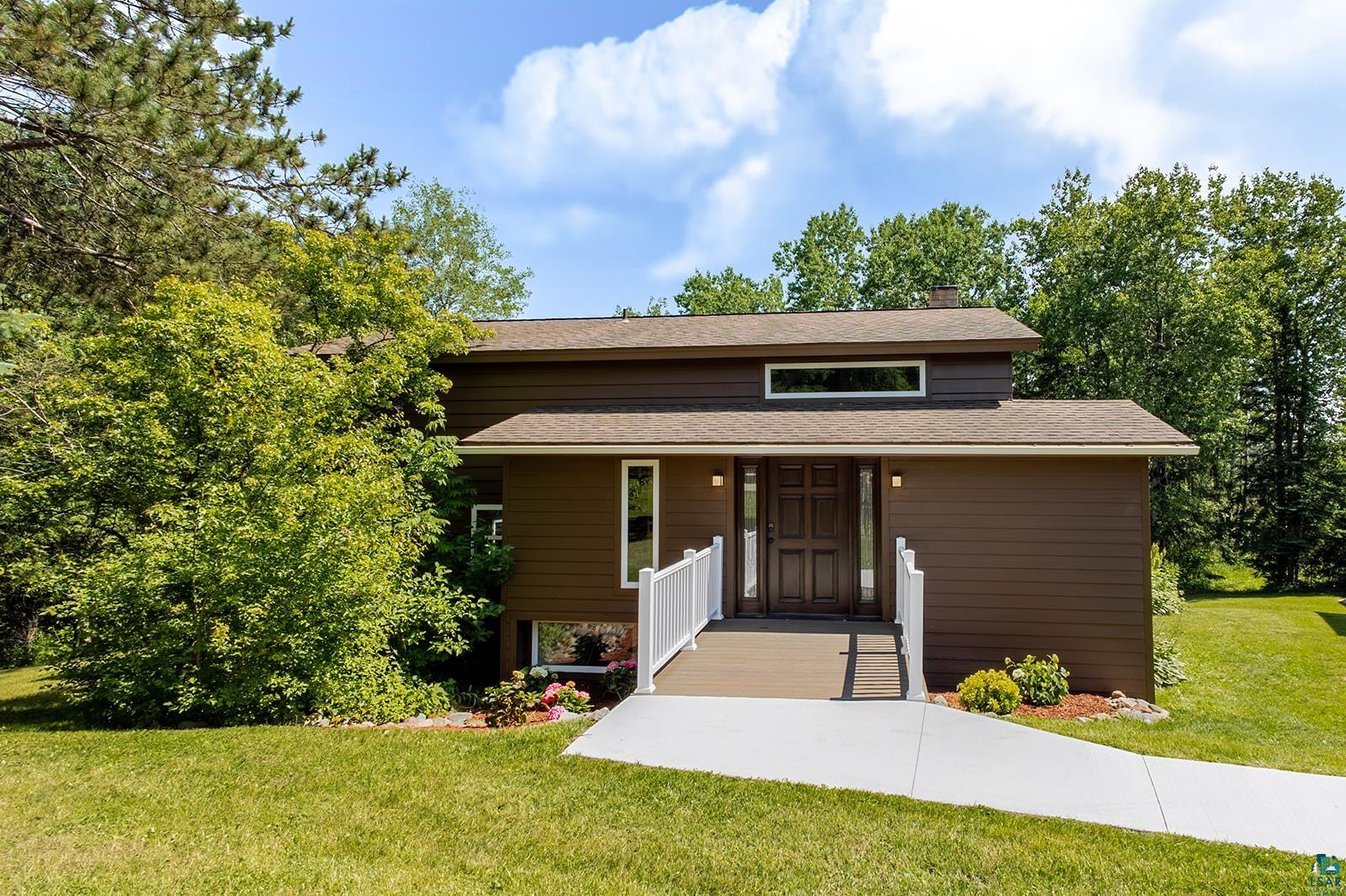 29 Ridge Road Esko, MN 55733 - Photo 2 of 41 Contemporary brown siding residence featuring a dark wood front door with sidelight windows, an integrated ramp with white railings, and a horizontal transom window above the entrance