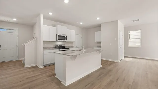 a kitchen with stainless steel appliances granite countertop a stove top oven a sink a refrigerator and white cabinets with wooden floor