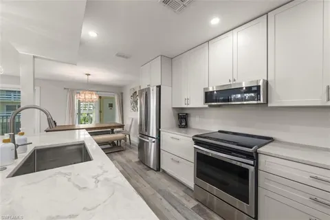 a kitchen with stainless steel appliances a stove a sink a refrigerator white cabinets and a wooden floor