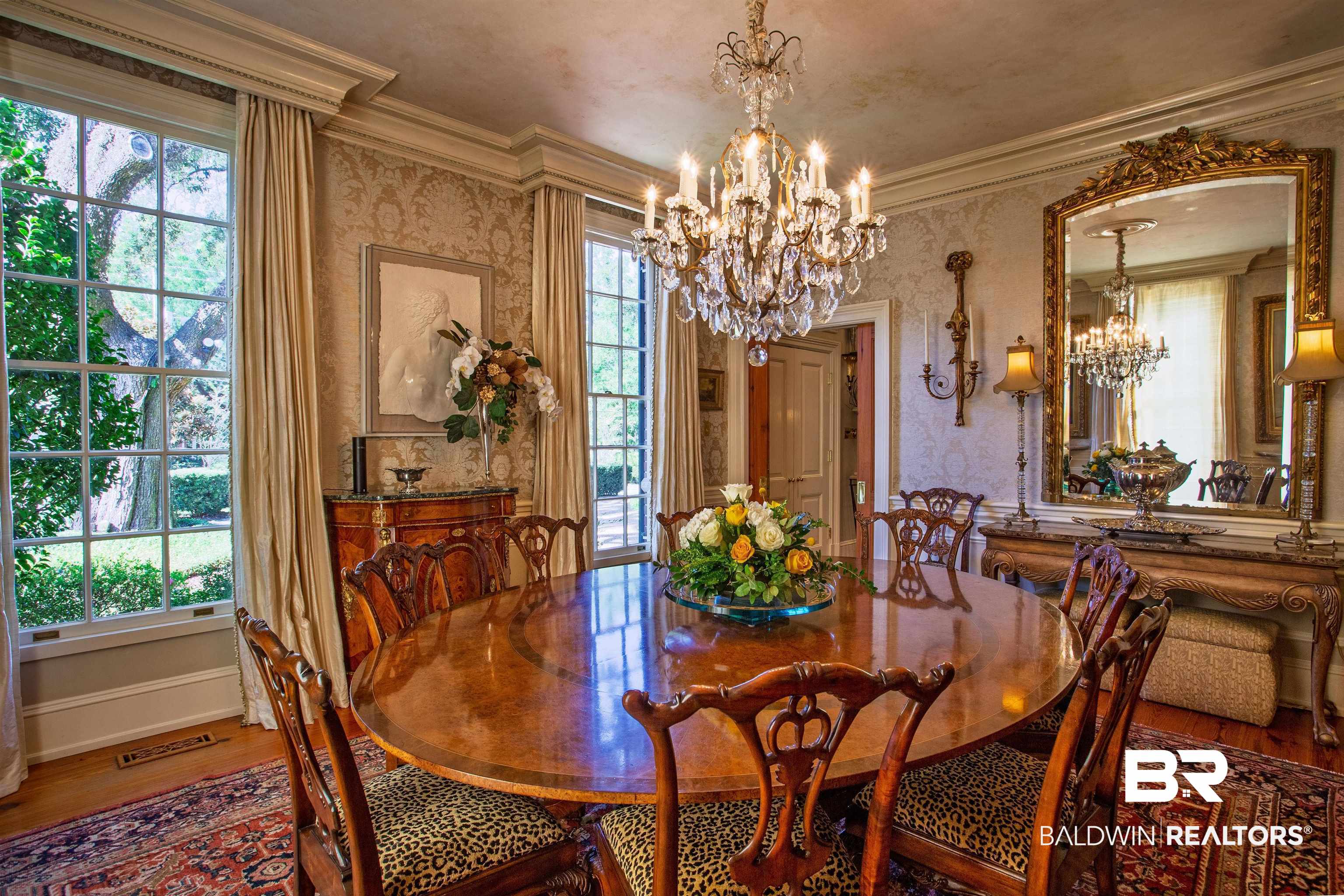 150 Austill Avenue Mobile, AL 36608 - Photo 13 of 39 Formal dining area featuring a prominent crystal chandelier, extensive crown molding, large paneled windows, patterned wallpaper, and wood-finish flooring