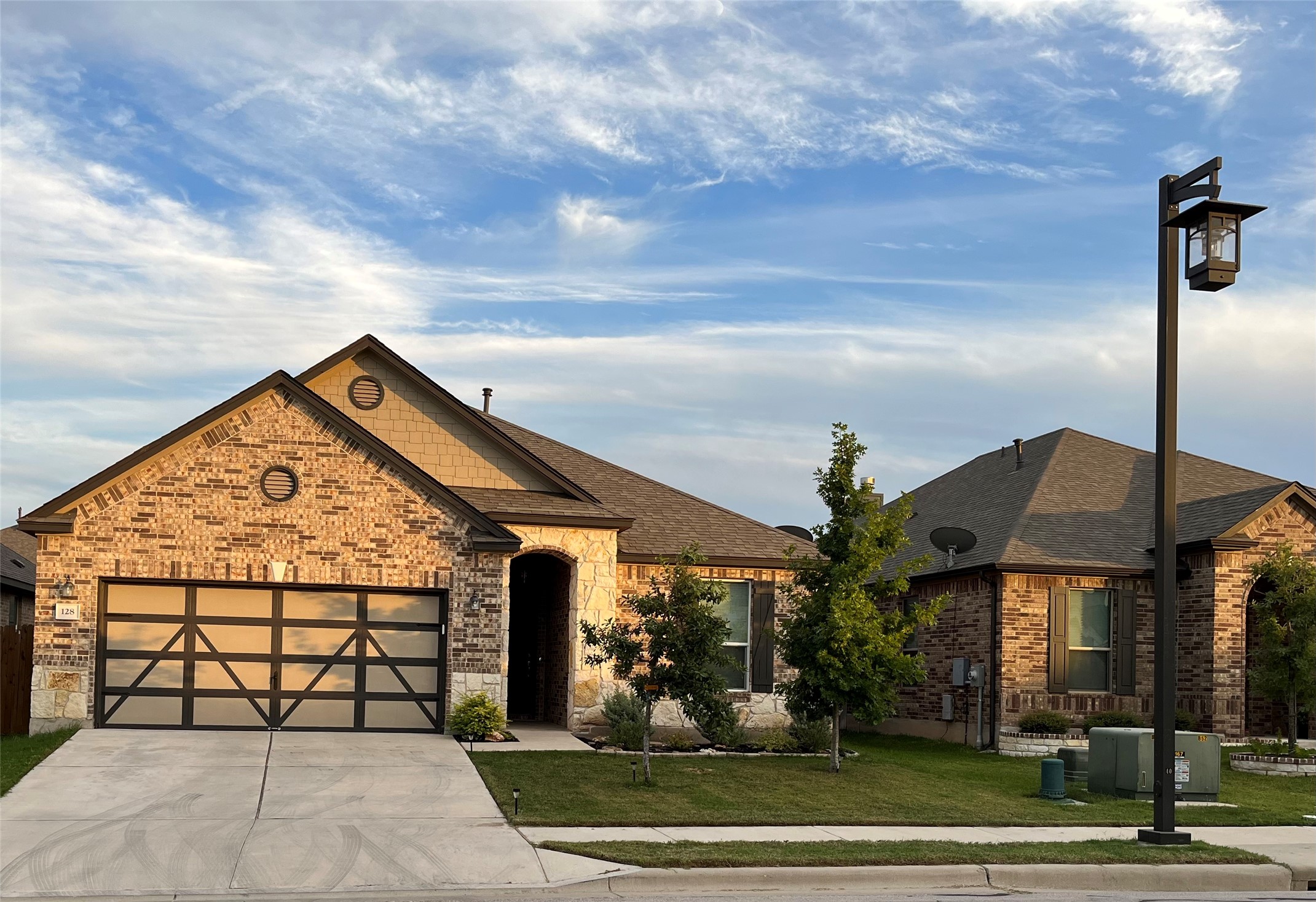 Brick and stone facade residence featuring a contemporary garage door with frosted panels, a concrete driveway, and mature landscaping