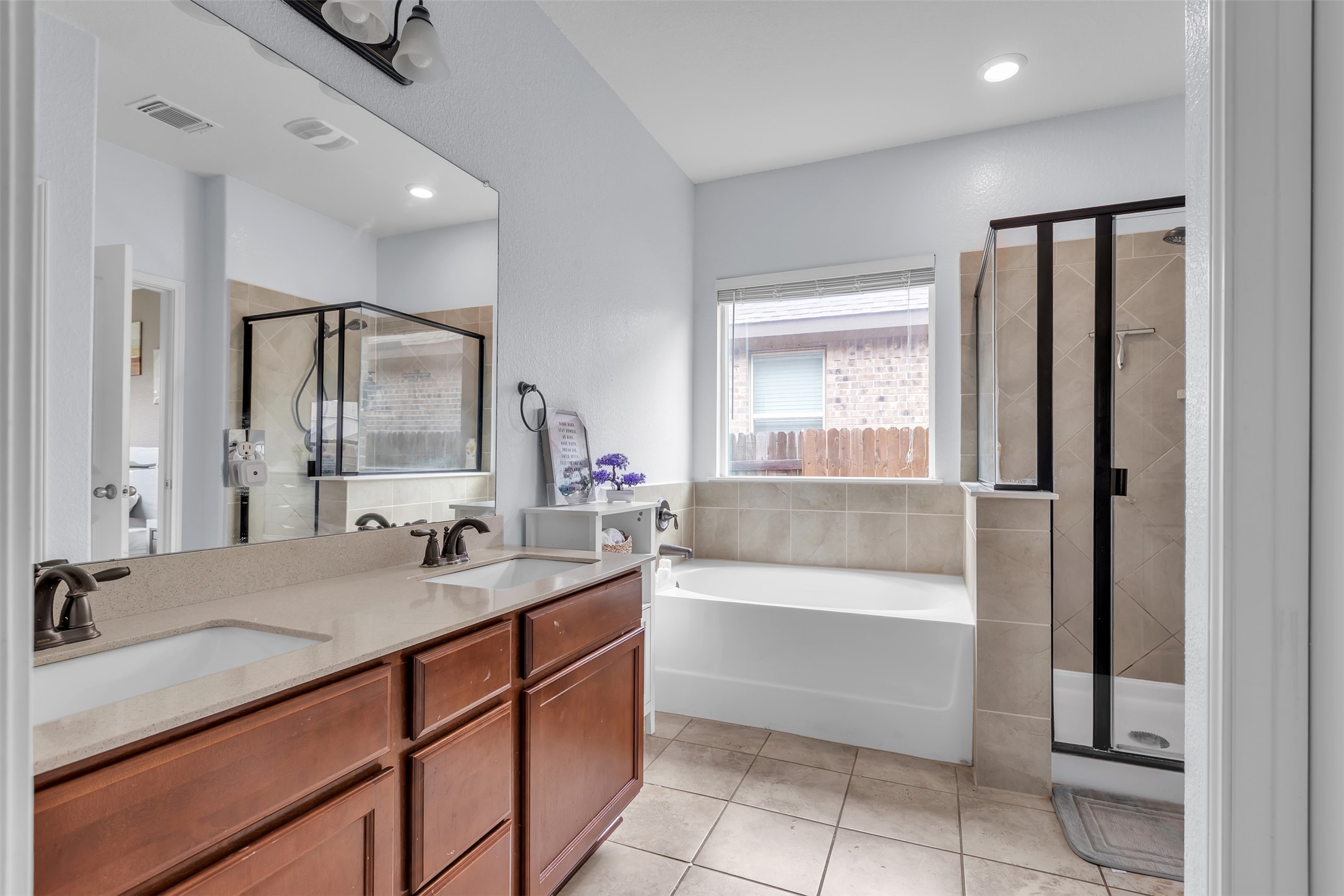128 Kavanaugh Street Georgetown, TX 78628 - Photo 10 of 13 Bathroom featuring a double vanity with stone-finish countertops, warm wood-finish cabinetry, a large built-in mirror, a built-in tub with tiled surround, and a separate glass-enclosed shower with tiled walls