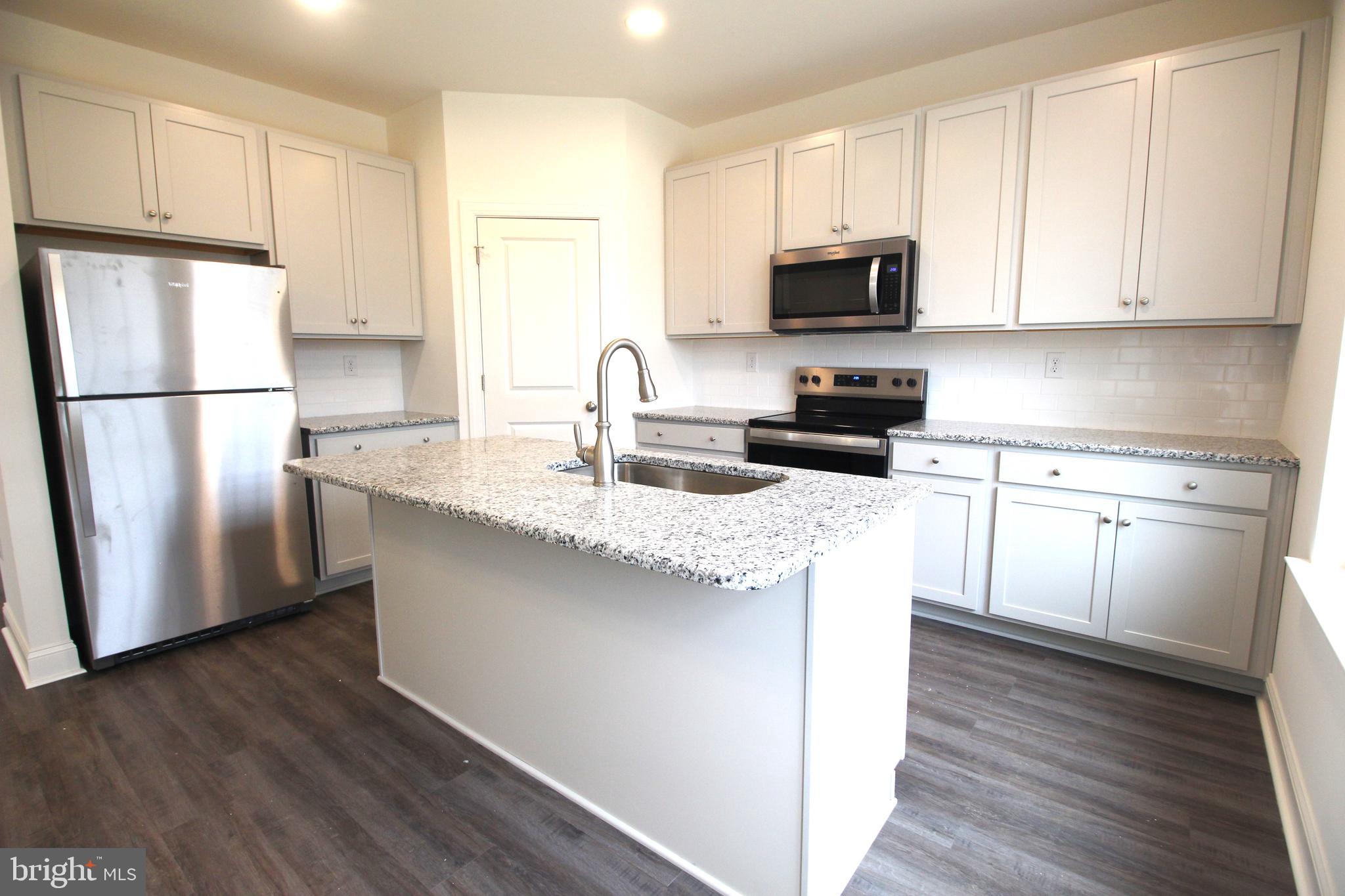851 Mapleton Avenue Middletown, DE 19709 - Photo 11 of 26 a kitchen with granite countertop a refrigerator stove a sink and white cabinets with wooden floor